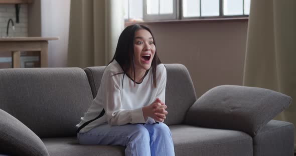 Happy Asian Young Woman Sit on Sofa and Watch TV Feels Excited Celebrating Online Lottery Victory