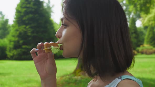 Girl Brunette Sitting in the Park and Eat a Sandwich with Salad