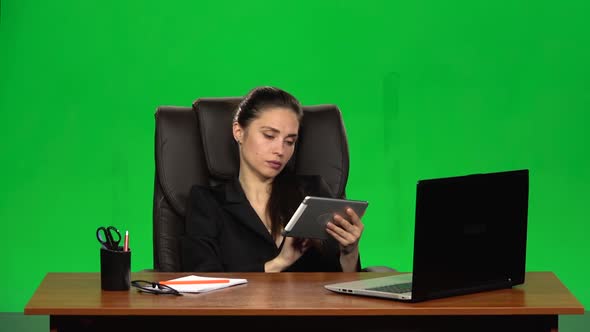 Worker Girl Sits at a Workplace Leaning Back in a Leather Chair and Communicates on a Tablet