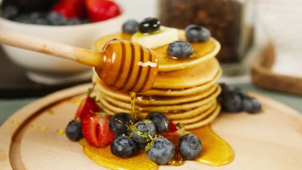 Pouring Honey or Maple Syrup on Pancakes with Berries on Top Closeup