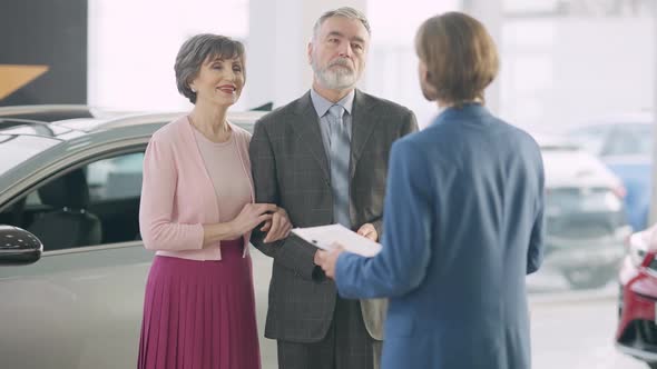 Portrait of Confident Wealthy Senior Couple Consulting Car Dealer in Showroom