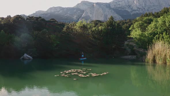 SUP Surfer Rows on Small Lake in Mountains