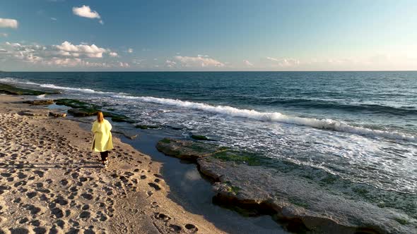 A girl in a yellow coat walks on the beach 4 K Aerial View