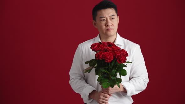 Sad Asian man in white shirt with a bouquet of red roses waiting for someone