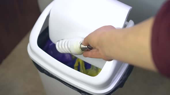 A woman throws broken fluorescent light bulb in a regular trash bin. Improper disposal electronics