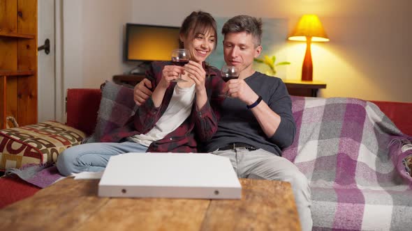 Couple Sits on Coach with Wine Glasses in Cozy Apartment at Evening