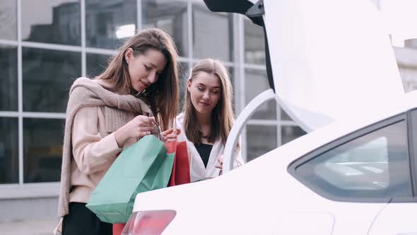 Happy Girlfriends Have Shopped and Putting Craft Shoppping Bags in a Car Trunk