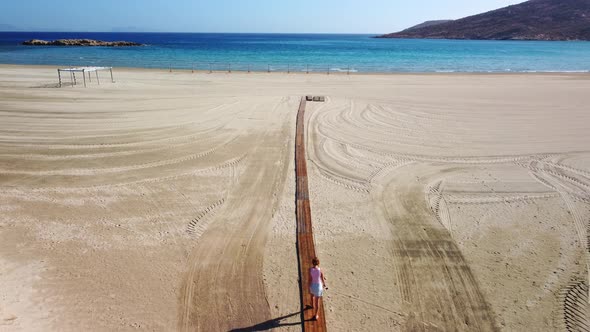 Beautiful romantic woman walking on wooden path to  the beach in summer vacation. Magganari beach. I