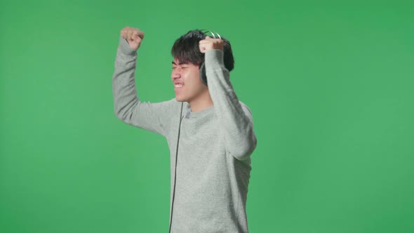 Side View Asian Man Listening To Music With Headphones And Dancing In The Green Screen Studio