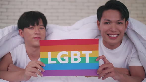 Happy gay Asian couple showing their love with rainbow flag.