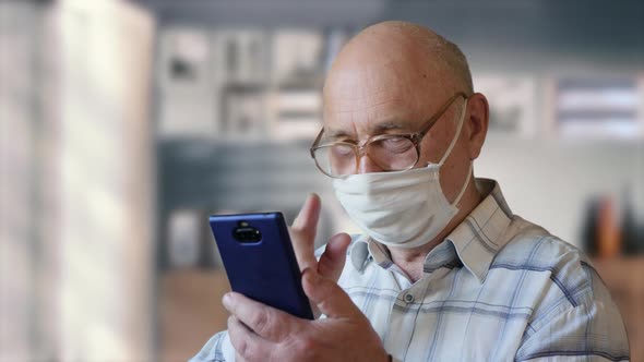 Old Man Reading News From a Smartphone at Home