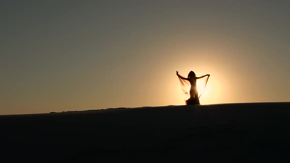 Brunette Veil in Her Hands Dancing Belly Dance on the Beach. Silhouette