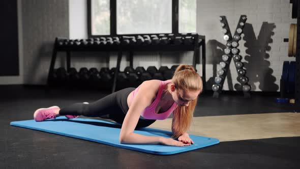 Young woman is training in the gym. In the plank, he does an exercise on the abs