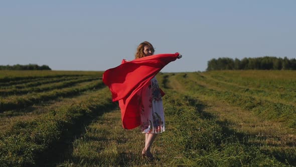 Redhead Woman in White Dress with Red Cloth in Her Hands on Background of Field