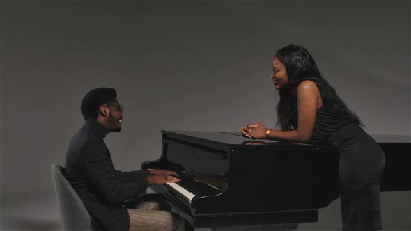 A Man in a Stylish Striped Suit Sings and Plays the Black Grand Piano for His Girlfriend. Happy