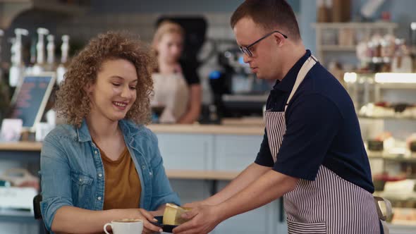 Caucasian male waiter with down syndrome serving a piece of cake in the cafe to the client at the ta