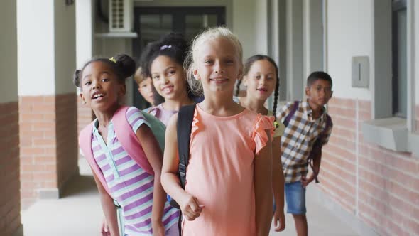 Video of happy caucasian girl and diverse pupils at schoot corridor