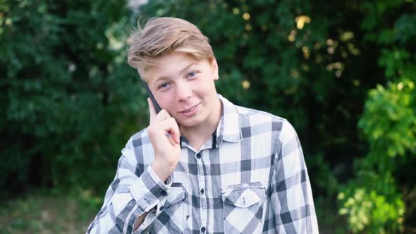 Young Caucasian Teenager Man in a Light Gray Checkered Shirt Speaks on the Phone