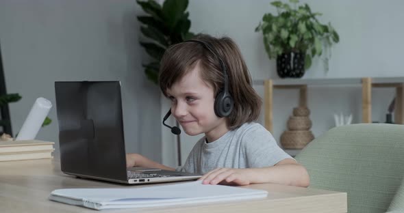 Enthusiastic Cute Boy Video Chatting Merrily Using Headset and Laptop with Friends and Parents