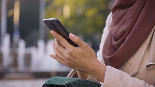 A Muslim Woman Works on a Smartphone in a Street in an Urban Area  a Fountain