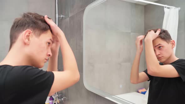 A Young Man in the Bathroom in Front of a Mirror is Styling His Hair