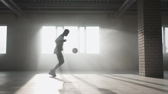A Black Guy Trains with a Soccer Ball in an Underground Parking Lot in the Sunlight in Slow Motion