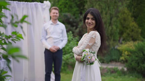 Back View of Happy Middle Eastern Bride Holding Wedding Bouquet Turning to Camera Smiling with