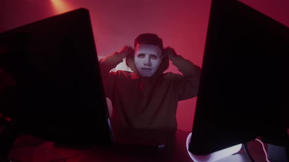 A Caucasian Man Puts on a White Mask Works on the Computer Inputs Code Types Very Fast on the