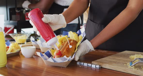 Mid section of african american woman wearing apron putting ketchup over hot dog in food truck