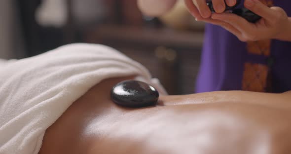 Masseur Puts Hot Stones on Back of Lying Young Attractive Cute Brunette Woman in Spa Center