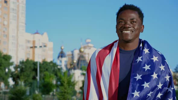 Smiling Afroamerican Man Walking Street with American Flag on Back in Summer