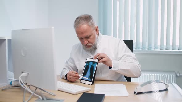 Grayhaired Male Doctor Sits at Workplace and Communicates with Patient Via Video Call the Doctor