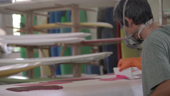 Asian Craftsman Painting Surfboard in Workshop