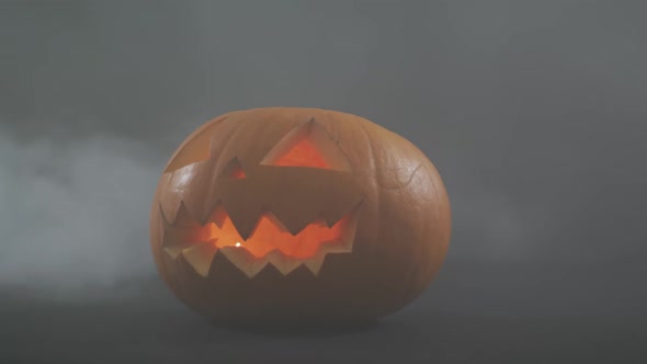 Smoke effect over scary face carved halloween pumpkin against grey background