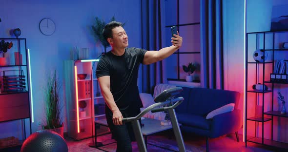 Asian Man in Sportswear Walking on Treadmill and Making Selfie During Evening Home Workout