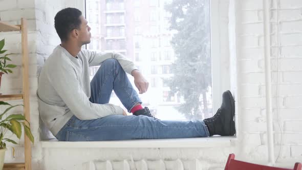 AfroAmerican Man Sitting at Window and and Looking Outside