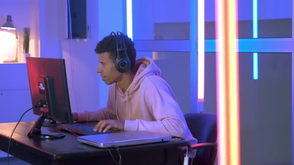 Persistent African Gamer Playing Online Shooter on Pc in Neon Room