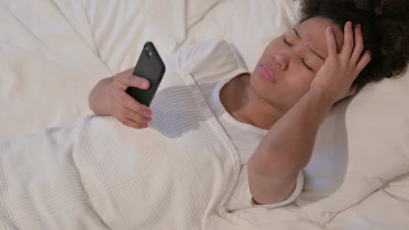 African Woman Reacts to Loss on Smartphone in Bed