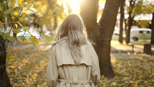 Rear View of an Elegant Woman Walking By Autumn Park in Trench Coat