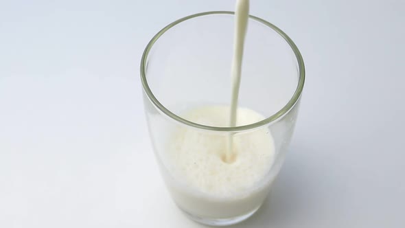 Pour the splash of milk into a clear glass on a white table.