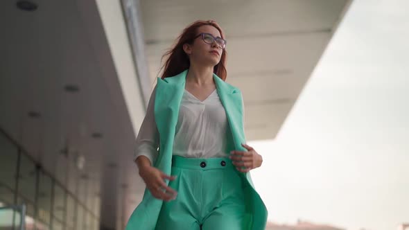 Beautiful confident business woman in glasses and a turquoise fashionable suit walks. Slow motion