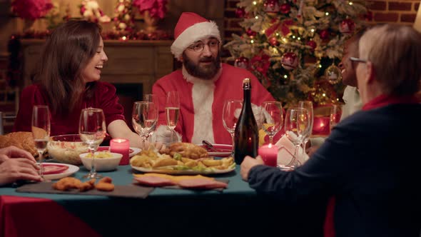 Funny Man Costumed As Santa Claus Talking with Family About Presents While at Christmas Dinner