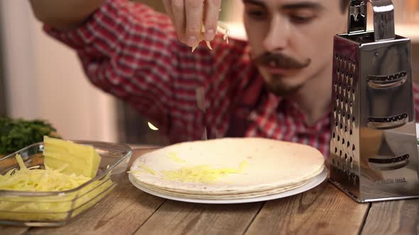 Closeup Footage of a Cook Who is Throwing Grated Cheese on Tortilla Lying on a Plate on Wooden Table