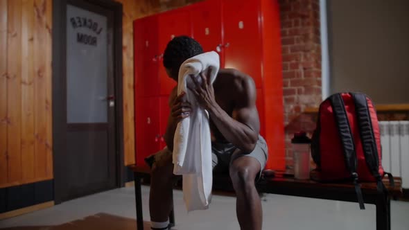 Africanamerican Athletic Young Man Wipes Off His Face with a Towel in Locker Room