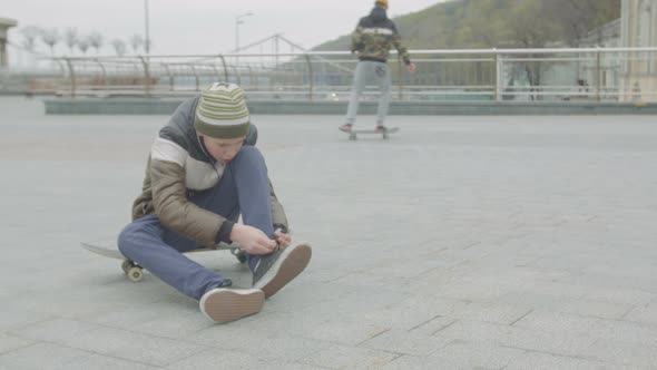 Teen Boy Tying Shoelaces Sitting on Skateboard