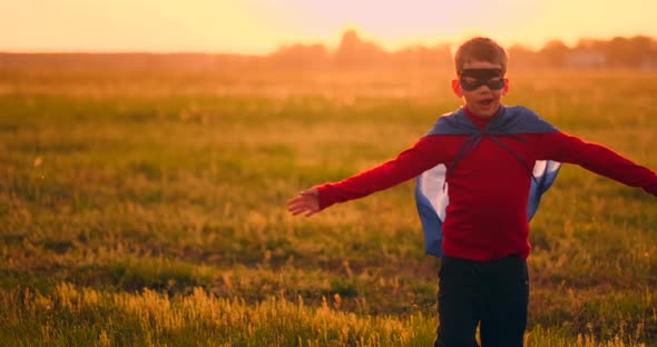 Boy in Superhero Costume and Mask Running Across the Field at Sunset Dreaming and Fantasizing