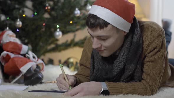 Concentrated Happy Adult Man Writing Letter To Santa Claus on Christmas Eve at Home