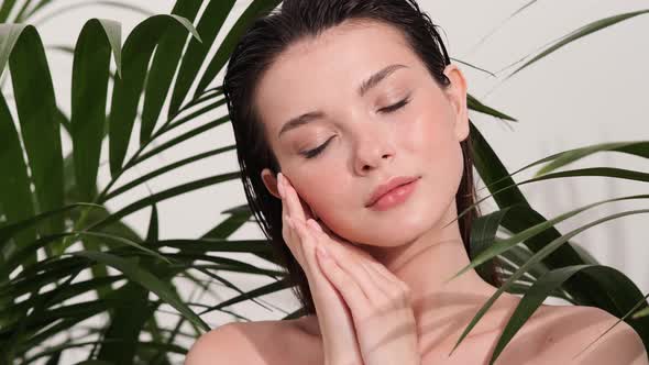 A beautiful brunette woman posing with tropical leaves while touching her neck