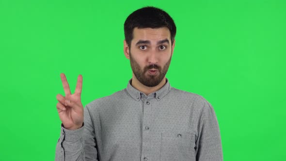 Portrait of Brunette Guy Is Showing Two Fingers Victory Gesture. Green Screen