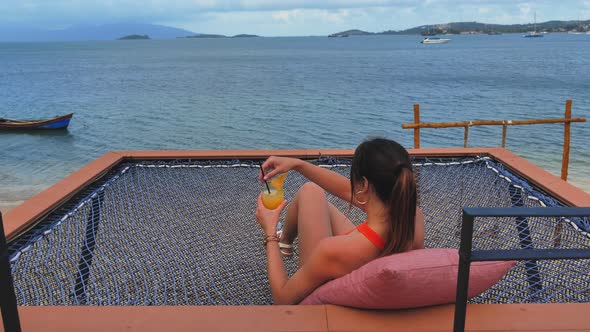 Woman Drinkig Fresh Smoothie on Beach in Hammock